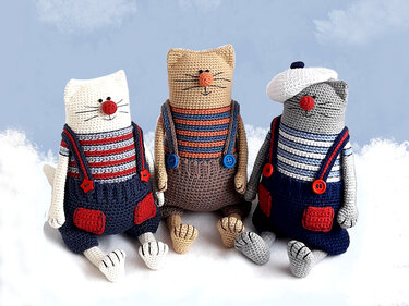 Three crocheted amigurumi cats in striped tops and overalls with button details