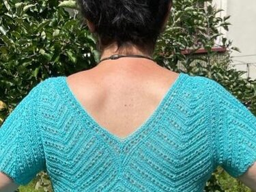 Rückenansicht einer Frau in einem türkisfarbenen, kurzärmeligen Strickshirt mit V-Rückenausschnitt und Zickzack-Lochmuster.
