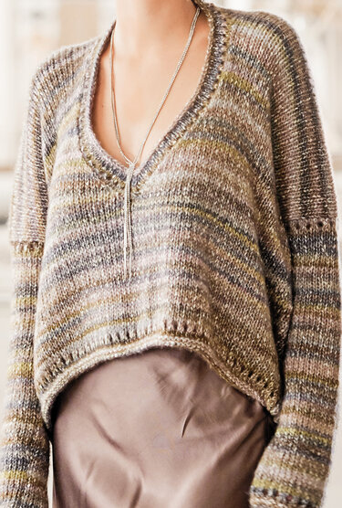 V-Ausschnitt-Strickpullover aus meliertem Garn in Braun-, Grau- und Grüntönen mit langer silberner Kette, Nahaufnahme bis zur Taille.