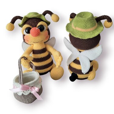 Gehäkelte Amigurumi-Biene mit grünem Hut, weißen Flügeln und Körbchen mit rosa Schleife