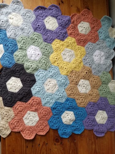 Crocheted baby blanket of flower-shaped hexagon motifs in assorted pastel and muted colors laid on a wooden floor