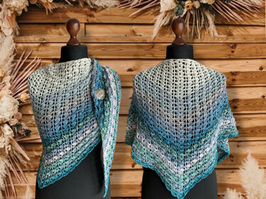 Zwei Mannequins präsentieren gehäkelte Dreieckstücher im Blau‑Grün‑Farbverlauf vor Holzpaneelen