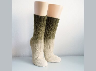 Pair of mid-calf knitted socks in an olive-to-cream gradient with a cable-lace cuff on foot forms