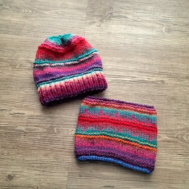 Gestrickte Kinder‑Mütze und passender Loop in buntem Farbverlauf auf Holzboden