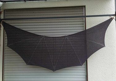 Gehäkeltes dunkles Halbrundtuch mit flügelartigen Bögen, vor einem geschlossenen Rollladen präsentiert