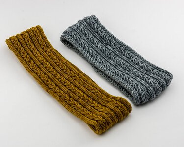 Nahaufnahme von zwei gestrickten Stirnbändern mit Zopfmuster in senfgelb und grau