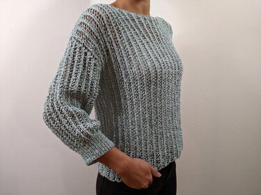 Seitliche Ansicht eines salbeigrünen Damenpullovers mit lockerem Ajour‑Lochmuster und schmalen Bündchen