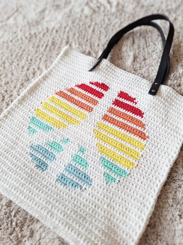 Weiße gehäkelte Shopper-Tasche mit bunten, gestreiften eiförmigen Motiven und schwarzen Henkeln