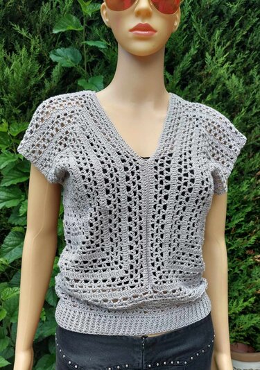 Grau gehäkeltes Kurzarm-Top mit V‑Ausschnitt an einer Schaufensterpuppe vor grünem Hintergrund.