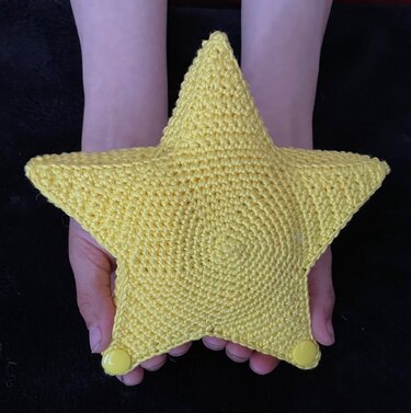 Gelbes gehäkeltes Sternkissen, in zwei Händen gehalten