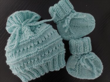 Gestrickte Baby-Mütze mit Kordel und zwei Schühchen in Mint auf dunklem Untergrund