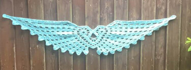 Mintgrüner gehäkelter Tischläufer mit offenem Wabenmuster und gezackter Kante, horizontal vor Holzbrettwand