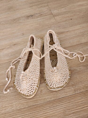 Paar gehäkelter naturweißer Ballerina-Schuhe mit Schnürbändern und Perlen auf Holzfußboden