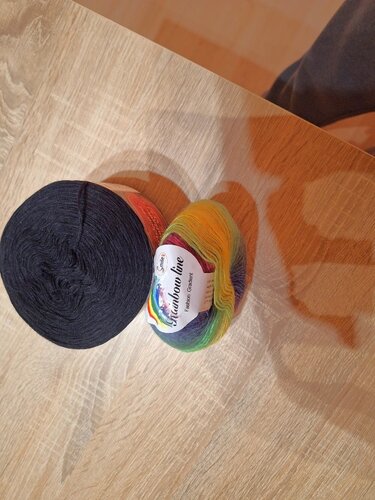 Zwei Garnknäuel auf Holz: ein mehrfarbiger Verlaufsbobbel und ein einfarbig dunkles Garn