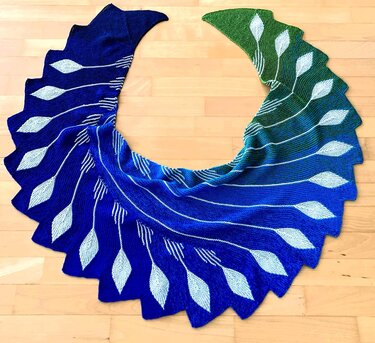 Halbmondförmiger Drachenschwanz‑Schal in Blau und Grün mit hellen Blattmotiven und gezacktem Rand