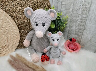 Zwei graue gehäkelte Amigurumi‑Mäuse, groß und klein, mit rosa Akzenten vor texturiertem Hintergrund und Deko