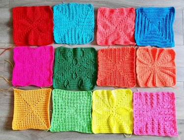 Zwölf bunte gehäkelte Quadrate auf Holzboden.