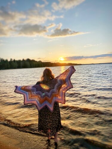 Person seen from behind wearing a chevron star crochet shawl at a lakeshore sunset