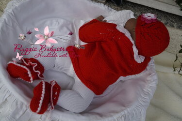 Baby liegt in rotem gestrickten Set mit Mütze, Jacke und Schühchen