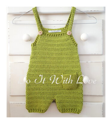 Lindgrüner gehäkelter Baby-Overall mit Trägern, zwei Holzknöpfen und einer kleinen Tasche an einem Drahtbügel