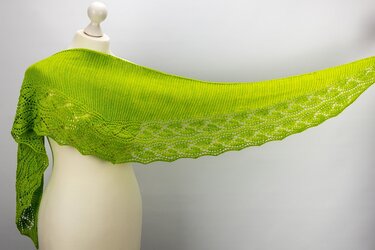 Bright green knitted shawl with decorative lace border and scalloped edge draped on a white mannequin.