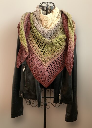 Gradient crochet triangle shawl in cream, gray, olive and rose draped on a mannequin wearing a black leather jacket