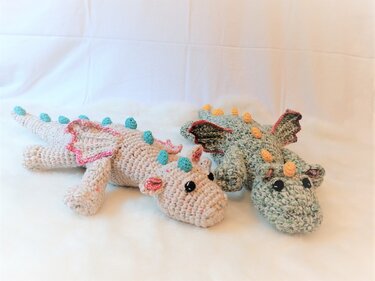 Zwei gehäkelte Amigurumi-Drachen, beige-rosa und meliert grün, auf weißem Untergrund.