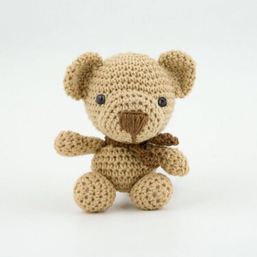 Beiger gehäkelter Amigurumi-Teddybär mit brauner Nase und Schal vor weißem Hintergrund