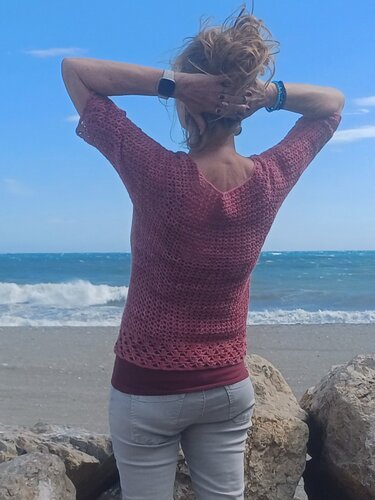 Rückansicht eines gehäkelten Kurzarm‑Shirts mit offenem Muster und Saumborte am Meer