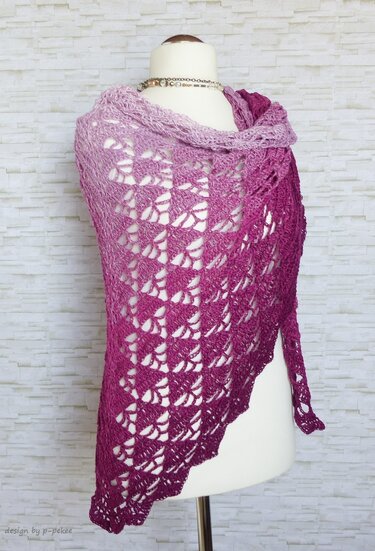 Gehäkeltes Dreieckstuch in Lila‑ und Pinktönen mit Lochmuster auf einer Schneiderpuppe vor heller Steinwand