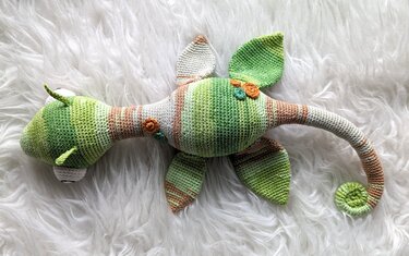 Gehäkeltes Seepferdchen-Amigurumi in grün-beigen Streifen auf weißem flauschigem Untergrund