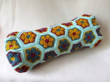 Gehäkelter Kissenbezug aus sechseckigen African‑Flower‑Motiven in Türkis, Senfgelb und Bordeaux