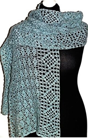 Hellblauer gehäkelter Schal mit offenem Lochmuster auf schwarzer Schneiderpuppe drapiert.