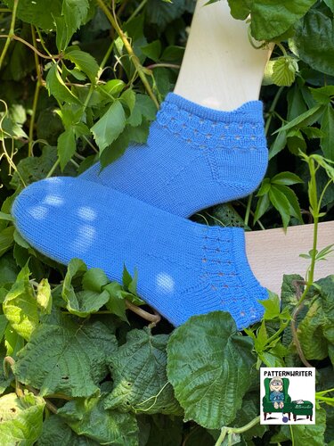 Detailaufnahme kurzer blauer Damensocken mit filigranem Lochmuster am Bündchen auf Schuhformen vor grünem Laub.