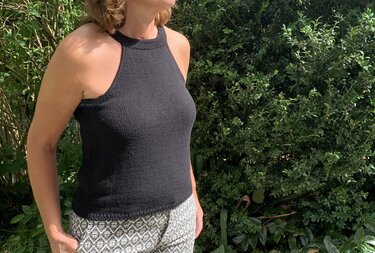 Schwarzes, hochgeschlossenes gestricktes Top mit Rippbündchen, getragen von einer Person vor grünem Hintergrund