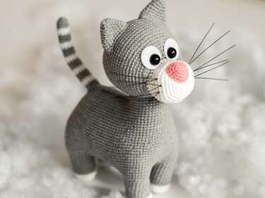 Gehäkelte graue Katze mit weißer Schnauze, rosa Nase, schwarzen Augen und gestreiftem Schwanz