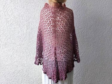 Rückenansicht eines halbrunden gehäkelten Tuchs in Rosa-Violett mit Lochmuster und gewelltem Abschluss