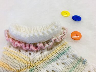 Gestrickte Socke mit Rüschenrand und Lochmuster in Pastellfarben, daneben bunte Knöpfe