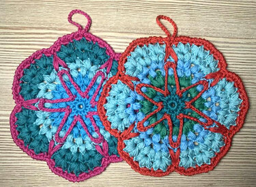 Zwei gehäkelte Topflappen in Blumenform mit bunten Rändern auf Holzhintergrund