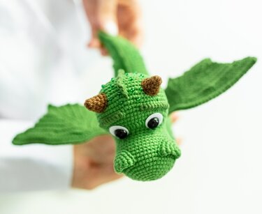 Close-up of green amigurumi dragon showing stitches, wings, and horns