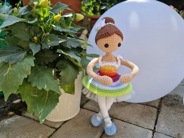 Gehäkelte Amigurumi-Ballerina mit Dutt, Regenbogen-Tutu und hellblauen Ballettschuhen auf Terrasse