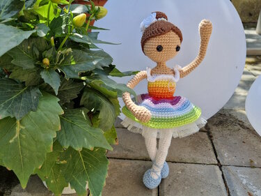 Gehäkelte Amigurumi-Puppe als Ballerina mit Regenbogenrock, weißer Blüte im Haar, weißen Beinen und blauen Schuhen