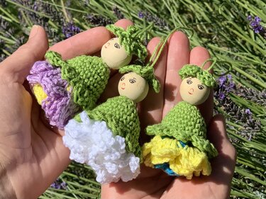 Mehrere kleine handgehäkelte Blumenfiguren mit Holzköpfen in einer Hand vor Lavendel