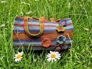 Gehäkelte, gestreifte Tasche mit Blumenapplikationen im grünen Gras