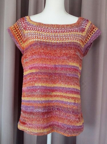 Gehäkeltes Damen-Shirt mit kurzen Ärmeln und bunten Streifen (Orange, Pink, Gelb, Lila) auf einer Schneiderpuppe.