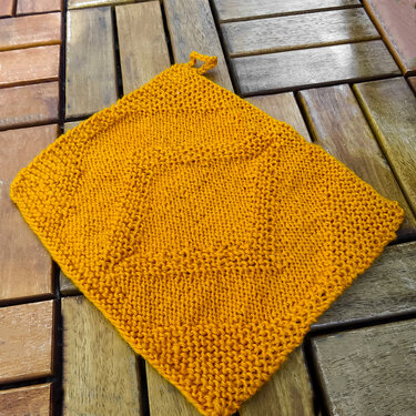 Orangefarbener gestrickter Topflappen mit Schlaufe auf Holztisch