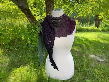 Mannequin wearing an asymmetrical crochet shawl with ribbed top and lacy tapered point in green, plum and black