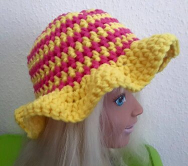 Gehäkelter gelb-pinker Hut mit welligem Rand auf einer Schaufensterpuppe