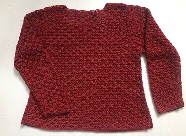Roter gehäkelter Damenpullover mit Muschelmuster, flach auf hellem Untergrund