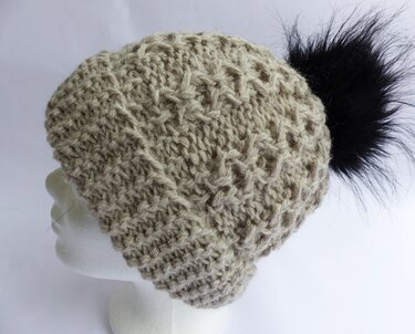 Beige gestrickte Mütze mit strukturierter Maschenarbeit und schwarzem Bommel auf Schaufensterkopf